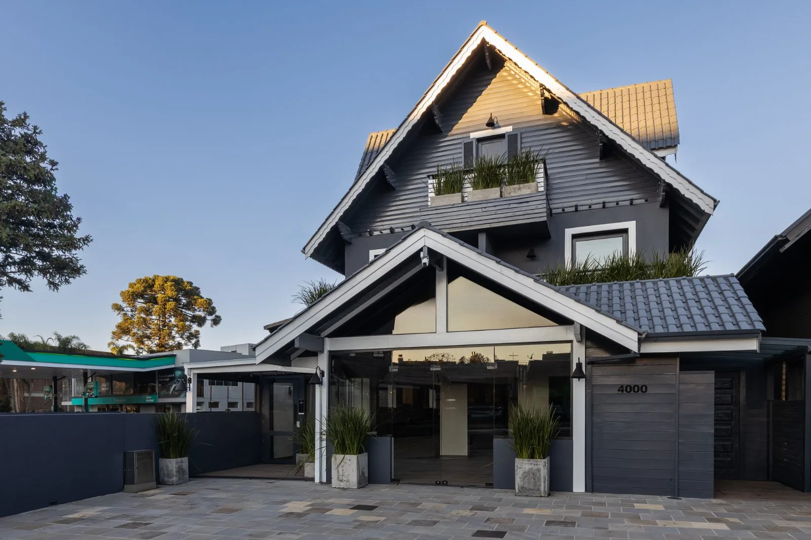 Fachada da pousada ao entardecer, com entrada de vidro iluminada e pátio de acesso