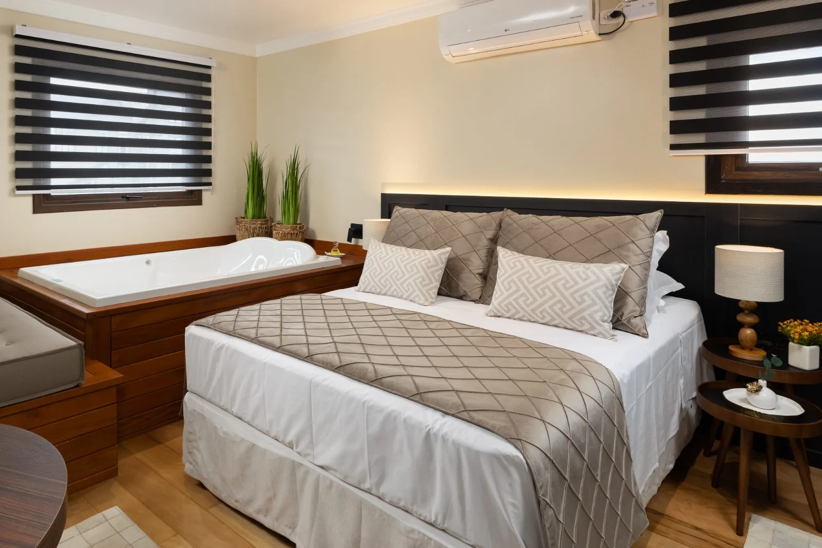 Cama de casal ao lado da banheira de hidromassagem, em suíte com piso de madeira
